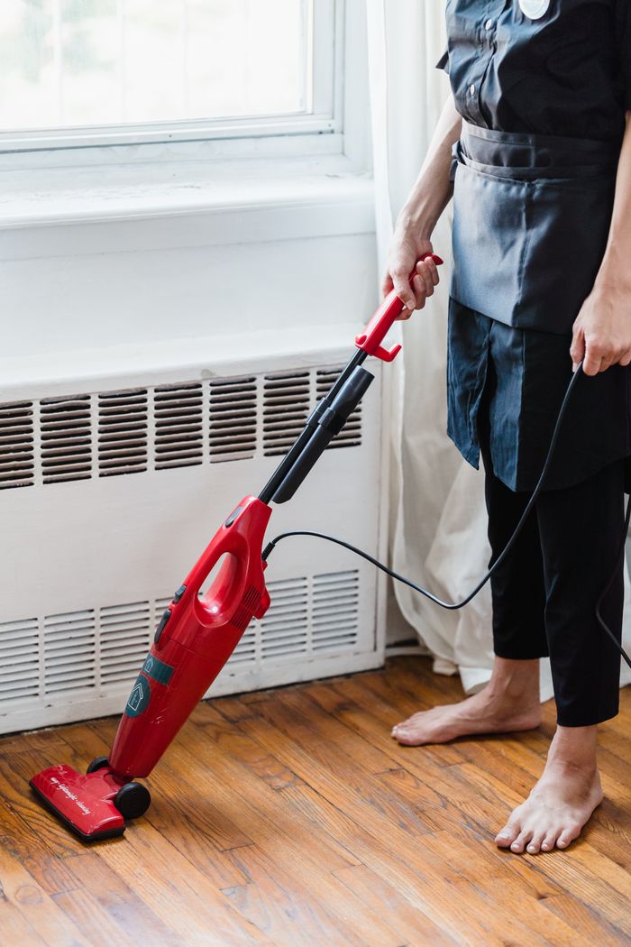 who-we-are Person cleaning wooden floor with red vacuum cleaner in a well-lit room.